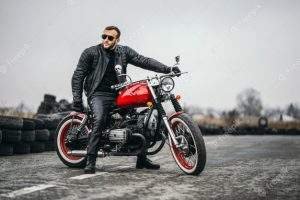 red-motorbike-with-rider-man-black-leather-jacket-pants-stands-sideways-middle-road_90153-1279